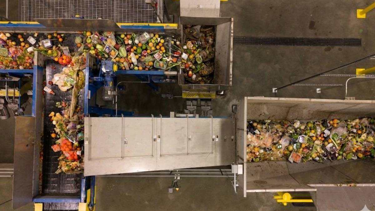 Top-down view of a waste-sorting facility with multiple conveyor belts and heaps of mixed recyclables and trash on a metal chute system.
