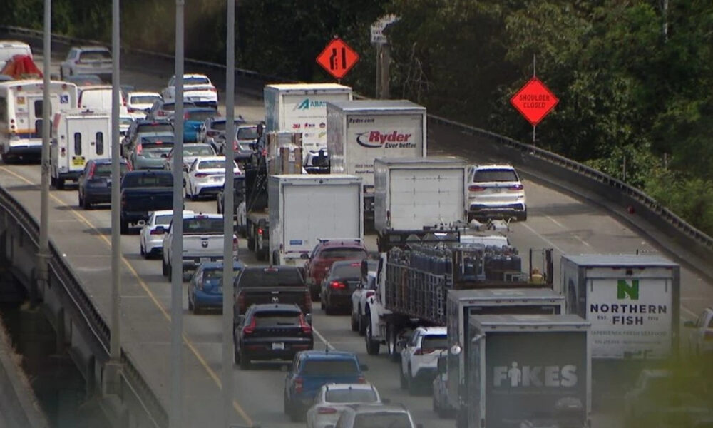 Heavy traffic on a multi-lane highway with construction signs and a closed shoulder on the road edge.