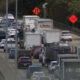 Heavy traffic on a multi-lane highway with construction signs and a closed shoulder on the road edge.