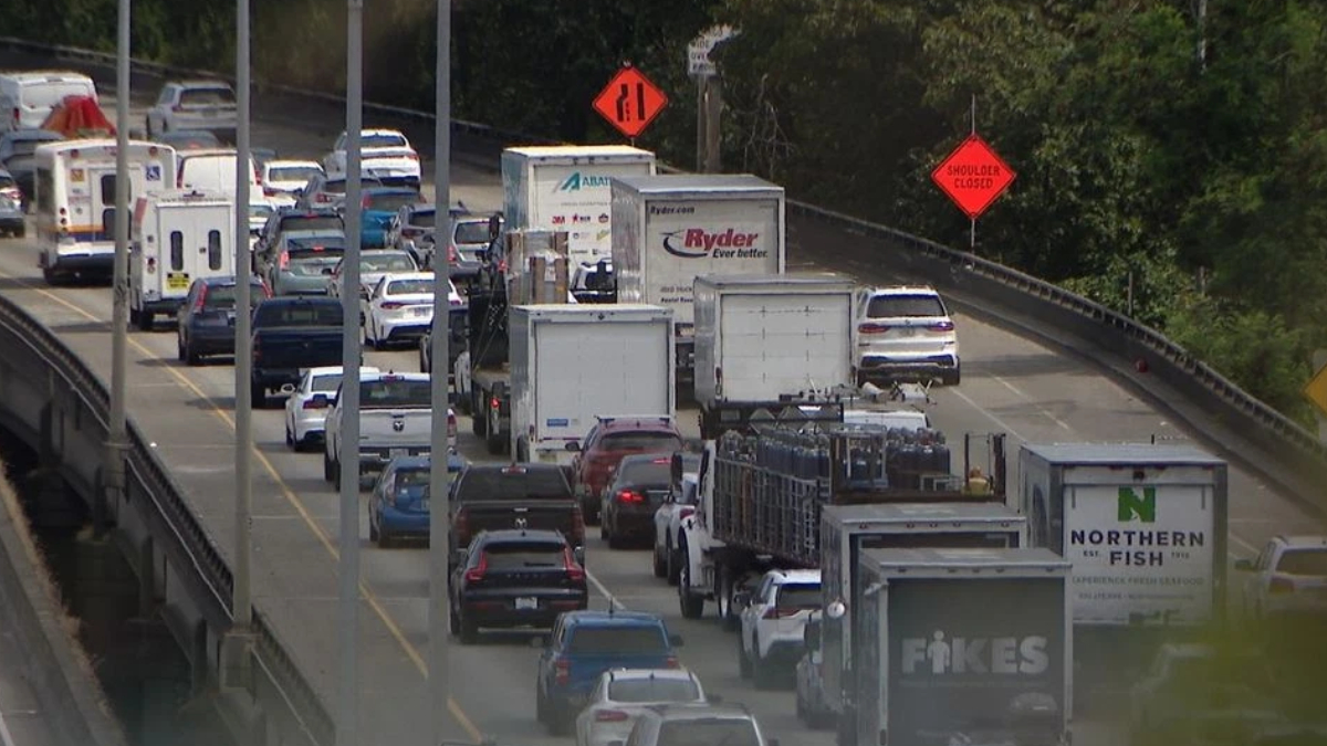 Heavy traffic on a multi-lane highway with construction signs and a closed shoulder on the road edge.