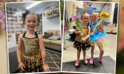 Young girl in a gold sequin dance dress standing in a backstage dressing room, smiling at the camera.
