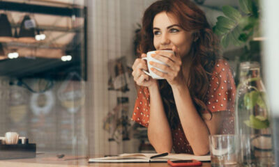 Woman in a red polka-dot blouse sipping coffee at a cafe table, with an open notebook nearby.