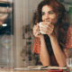Woman in a red polka-dot blouse sipping coffee at a cafe table, with an open notebook nearby.