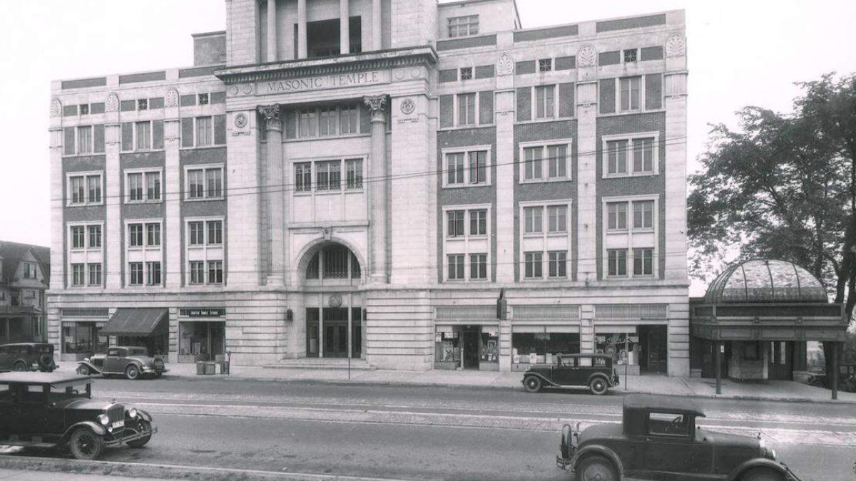 Historic street view of a large Masonic Temple building with arched entrance and decorative facade, early 20th-century cars parked along the curb.