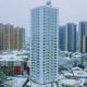 Snow-covered cityscape with a tall white residential tower surrounded by colorful high-rrise buildings.