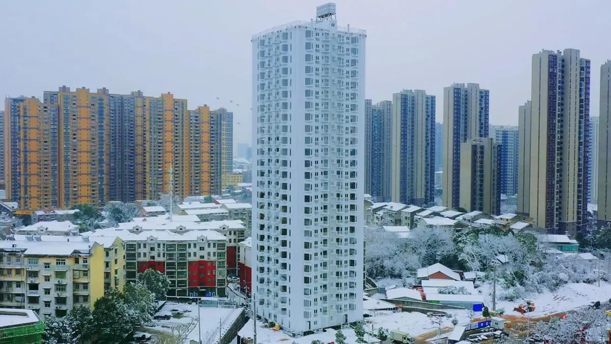 Snow-covered cityscape with a tall white residential tower surrounded by colorful high-rrise buildings.