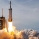 SpaceX rocket lifting off from a launch pad with bright flames and a plume of smoke rising around the rocket.