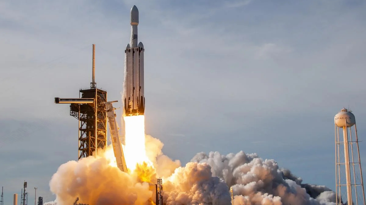 SpaceX rocket lifting off from a launch pad with bright flames and a plume of smoke rising around the rocket.