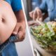 Split image: left side shows a pregnant belly with jeans unbuttoned; right side a person preparing a bowl of salad.