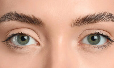 Close-up of a person's green eyes with well-groomed eyebrows and light makeup on peach-toned skin.