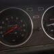 Close-up of a car dashboard with a speedometer and secondary gauges; the red needle sits near 0 mph, ready to drive.