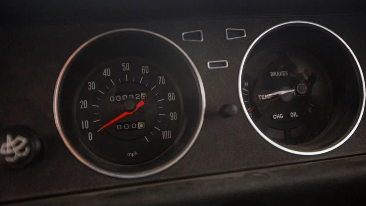 Close-up of a car dashboard with a speedometer and secondary gauges; the red needle sits near 0 mph, ready to drive.