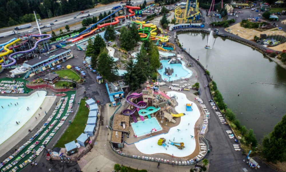 Aerial view of a bustling water park with colorful twisting slides, pools, and a surrounding lake.