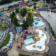 Aerial view of a bustling water park with colorful twisting slides, pools, and a surrounding lake.