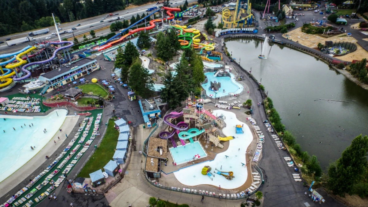 Aerial view of a bustling water park with colorful twisting slides, pools, and a surrounding lake.