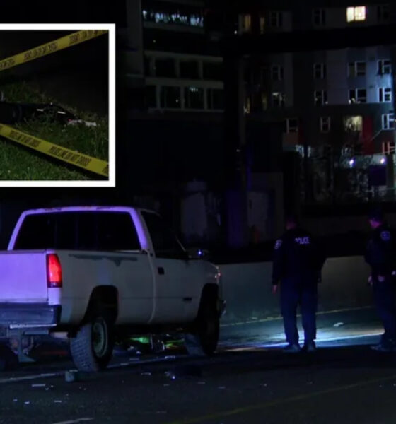 Nighttime crime-scene: a white pickup truck stopped on a street with police tape and two officers nearby, urban buildings in the background.
