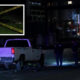 Nighttime crime-scene: a white pickup truck stopped on a street with police tape and two officers nearby, urban buildings in the background.