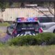 Seattle Police patrol car with red and blue lights on in a yard, parked behind a hedge and near an industrial backdrop.