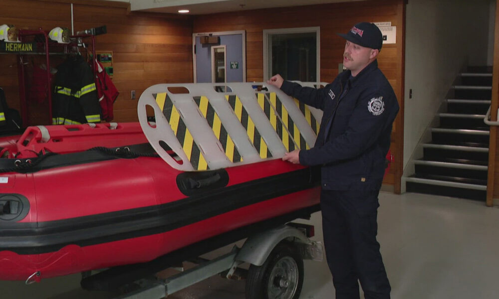 Firefighter in a dark uniform placing a striped safety barrier onto a red inflatable boat indoors.