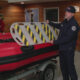 Firefighter in a dark uniform placing a striped safety barrier onto a red inflatable boat indoors.