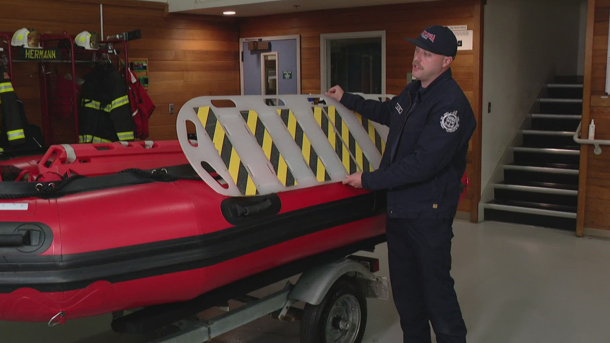 Firefighter in a dark uniform placing a striped safety barrier onto a red inflatable boat indoors.