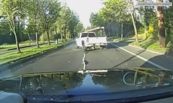 Dashcam view of a white pickup truck driving on a tree-lined residential street, seen from the hood of the observer's vehicle.