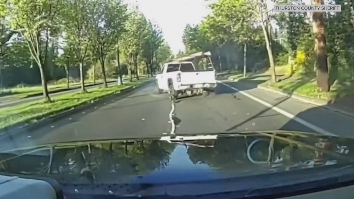 Dashcam view of a white pickup truck driving on a tree-lined residential street, seen from the hood of the observer's vehicle.