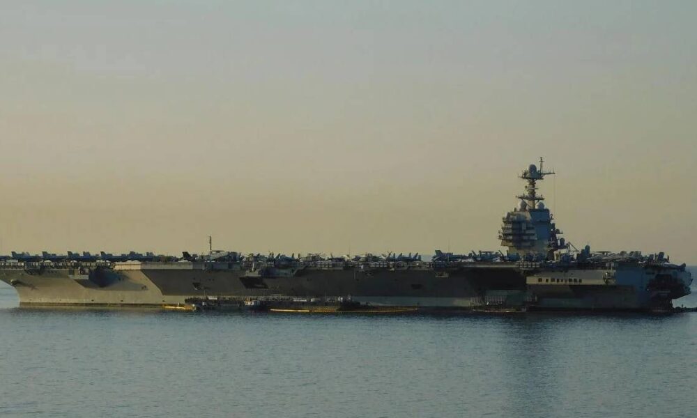 An aircraft carrier on calm water with numerous planes arranged on its deck at sunset.