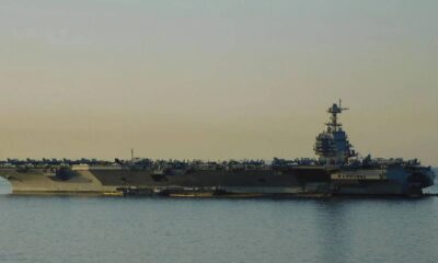 An aircraft carrier on calm water with numerous planes arranged on its deck at sunset.