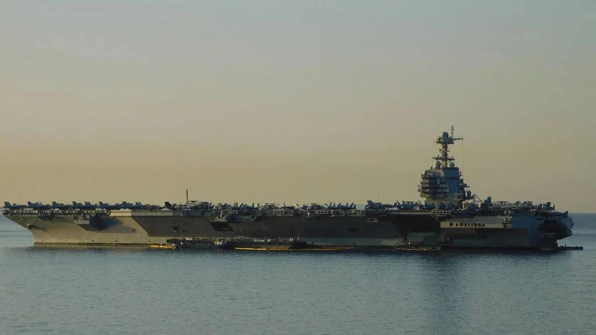An aircraft carrier on calm water with numerous planes arranged on its deck at sunset.