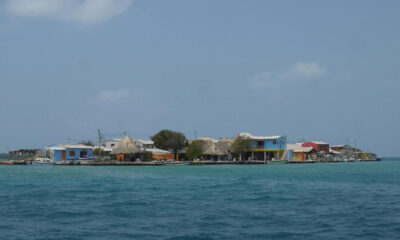 Small coastal village on a low-lying island with colorful houses and thatched roofs along a calm turquoise sea under a clear blue sky.