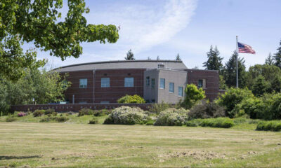 Municipal building with a brick exterior, a pale-gray entry tower, and an American flag on the right, surrounded by trees and a grassy lawn.