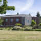 Municipal building with a brick exterior, a pale-gray entry tower, and an American flag on the right, surrounded by trees and a grassy lawn.