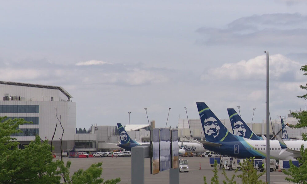 Airplanes with Alaska Airlines tails parked at a gate area of a sunny airport terminal.