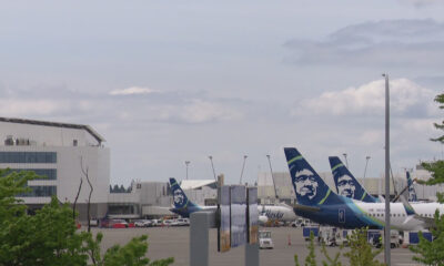 Airplanes with Alaska Airlines tails parked at a gate area of a sunny airport terminal.