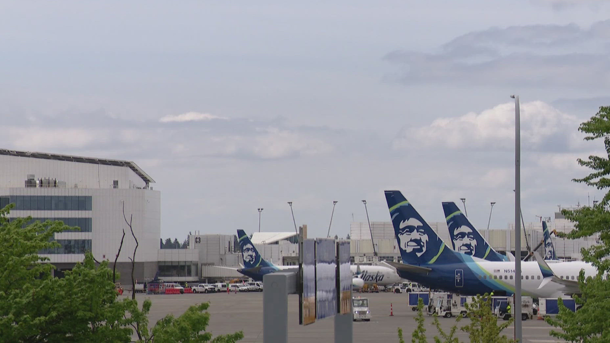 Airplanes with Alaska Airlines tails parked at a gate area of a sunny airport terminal.