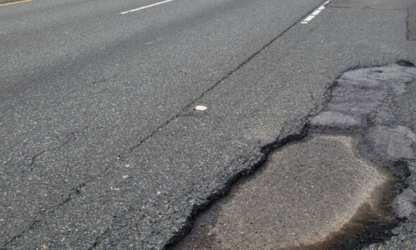 Pothole in a cracked asphalt road near the curb on the right side of the lane boundary gradually expanding into the pavement edge.