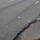 Pothole in a cracked asphalt road near the curb on the right side of the lane boundary gradually expanding into the pavement edge.