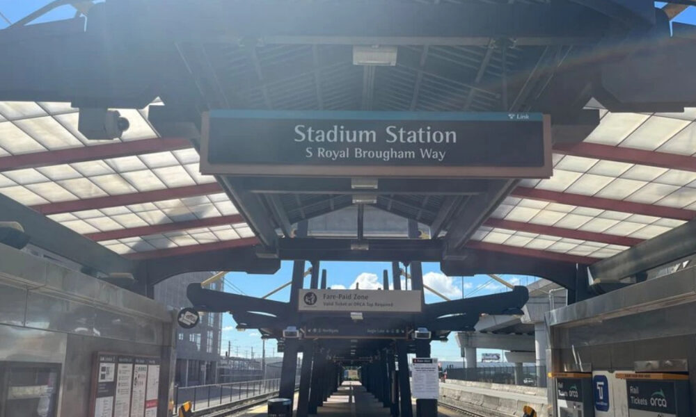 Platform at Stadium Station with a sign reading 'Stadium Station' and 'S Royal Brougham Way', view down the concourse under a glass canopy.