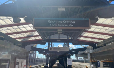 Platform at Stadium Station with a sign reading 'Stadium Station' and 'S Royal Brougham Way', view down the concourse under a glass canopy.