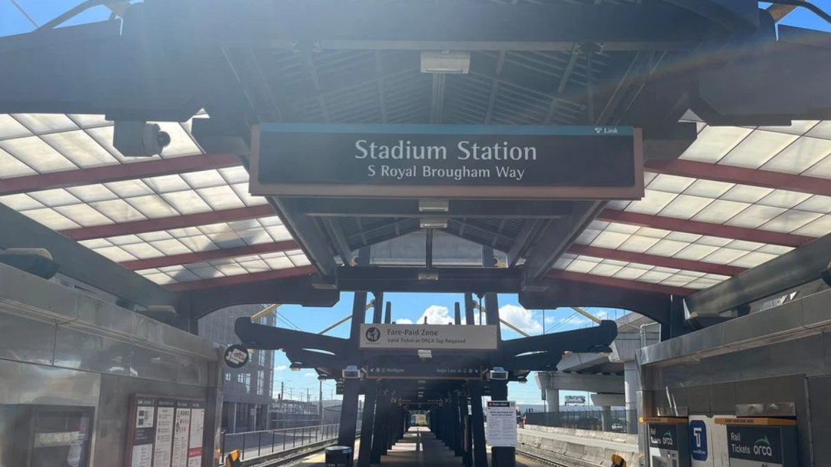 Platform at Stadium Station with a sign reading 'Stadium Station' and 'S Royal Brougham Way', view down the concourse under a glass canopy.