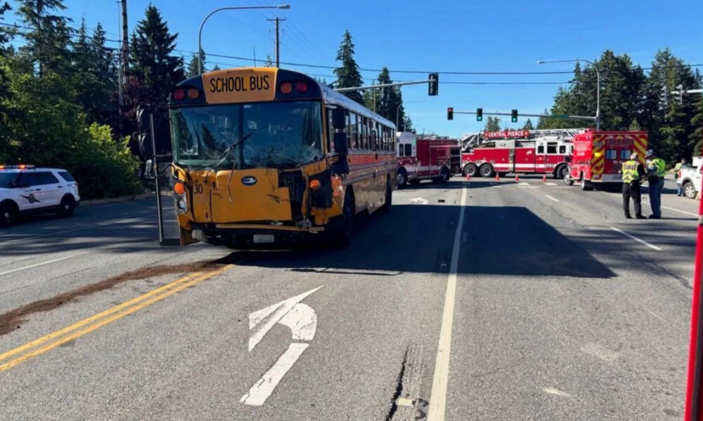 Yellow school bus with front-end damage blocking a street, surrounded by fire trucks and responders at an emergency scene.