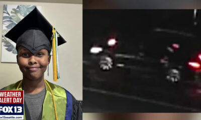 Young graduate in cap and gown posing indoors with a weather alert graphic at the corner and a green stole on, celebrating a milestone.