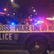 Police car with flashing lights behind yellow ‘Do Not Cross’ tape at night, indicating a crime scene.CTRL lines show police presence and blocked area.