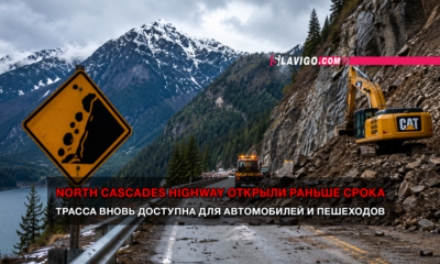 Mountain highway construction scene with a yellow CAT excavator on a rocky slope, warning sign, guardrail, and a banner announcing the North Cascades Highway opened early in red text.