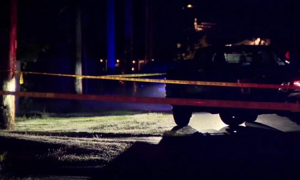 Nighttime street scene with police tape across the road, a dark SUV, and blue and red emergency lights.