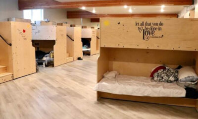 Dormitory-style shelter with wooden bunk beds along a hallway of a sunny, well-lit room.