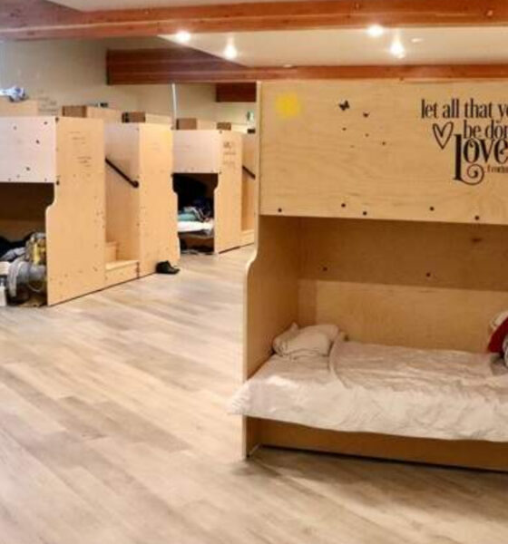 Dormitory-style shelter with wooden bunk beds along a hallway of a sunny, well-lit room.