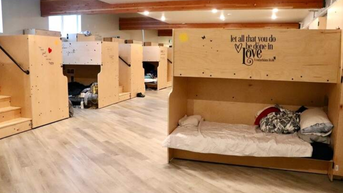Dormitory-style shelter with wooden bunk beds along a hallway of a sunny, well-lit room.