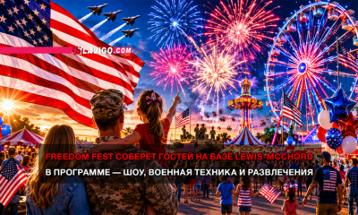 Patriotic festival scene at dusk with American flags, fireworks, a ferris wheel, and soldiers on stage; crowd of families celebrating Freedom Fest at Lewis-McChord base.